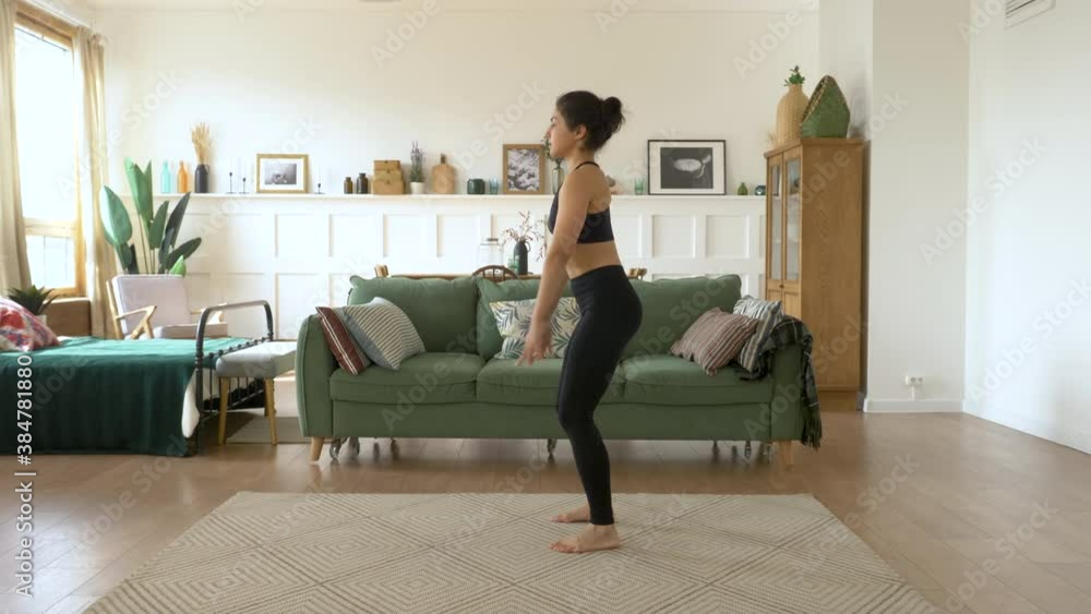 Strong Indian girl student is squatting at home standing on floor of beautiful light flat focused on exercise. Woman is wearing trendy leggings, short top Strong Indian girl student is squatting at home standing on floor of beautiful light flat focused on exercise. Woman is wearing trendy leggings, short top
