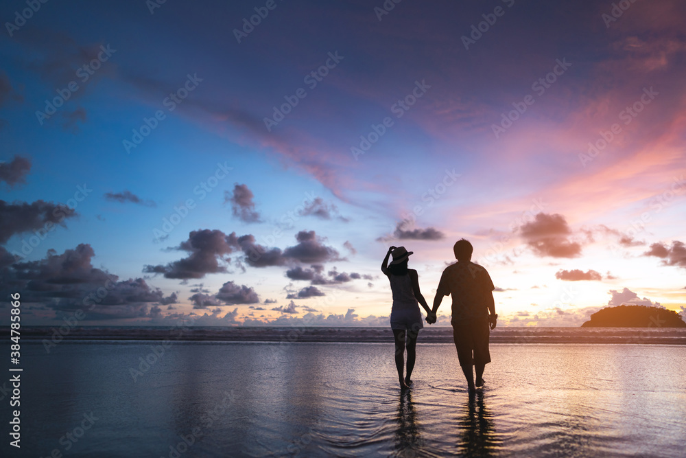 Rear view of adult tourist asian love couple holding hand on the beach with sunset sky background