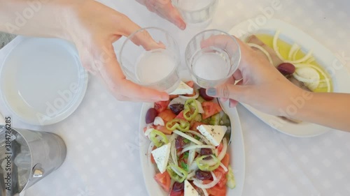 Group of friends toasting together at a restaurant top view. Social bonding with people clinking with glasses of alcoholic ouzo drink above a tavern table with Greek salad and fish meze starter food.