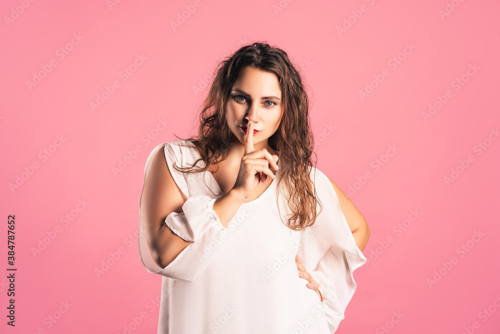 Hush, pize size model in white dress shows shh sign, fat woman having secret, pink background Hush, pize size model in white dress shows shh sign, fat woman having secret, pink background