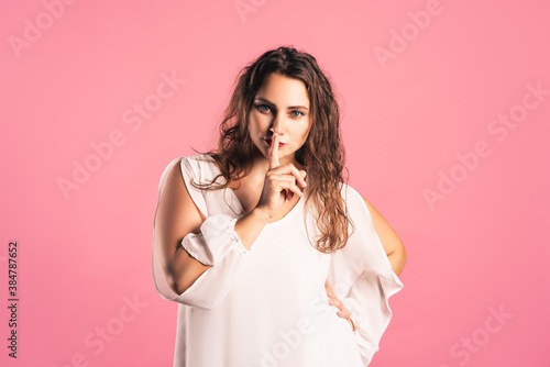 Hush, pize size model in white dress shows shh sign, fat woman having secret, pink background photo