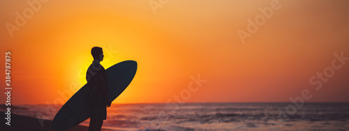 Silhouette of man surfer on the beach near the ocean watching sunset. Wide screen  panoramic