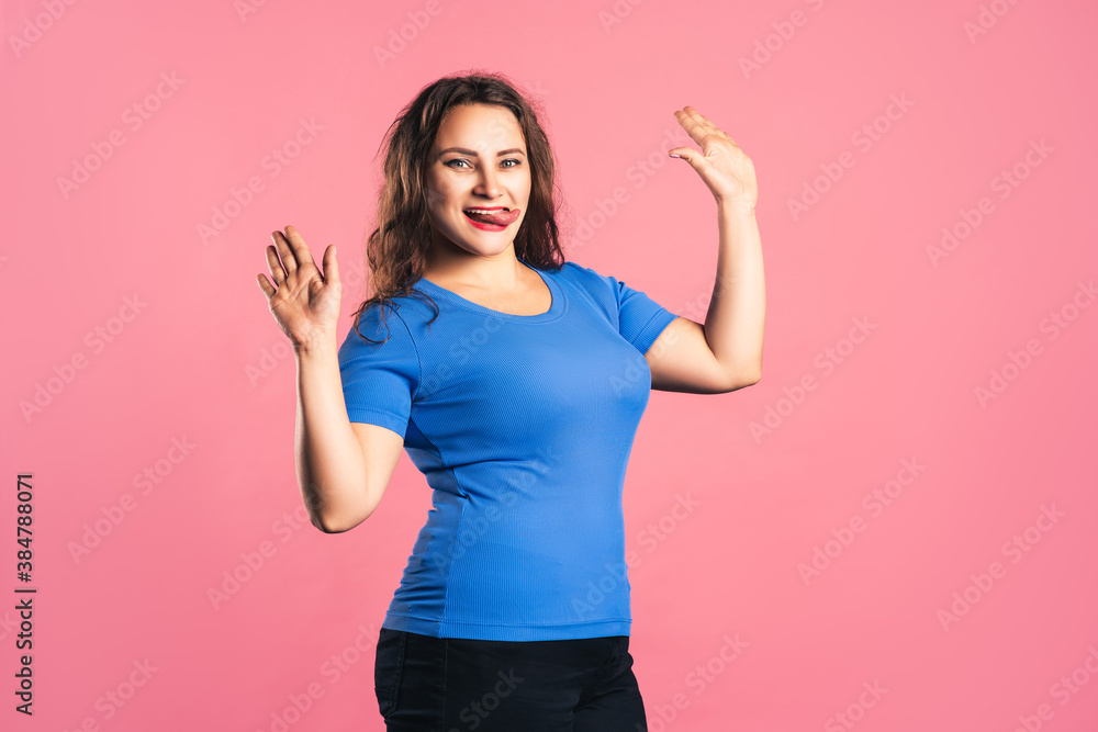 Happy plus size model in blue t-shirt showing tongue on pink background Happy plus size model in blue t-shirt showing tongue on pink background