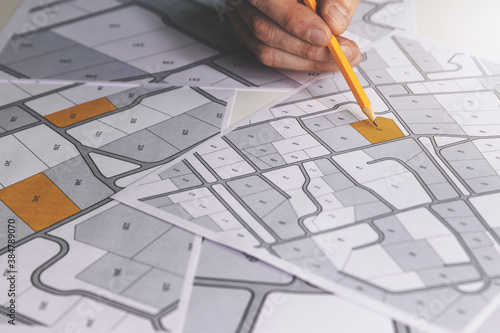 hand with pencil on cadastral map - choose and buy a building plot for house construction