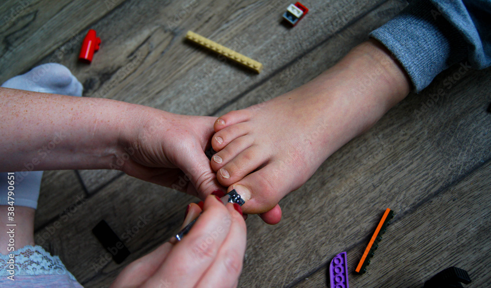 Mom cuts leg's nails her child with hand scissors on on the floor in the children's room