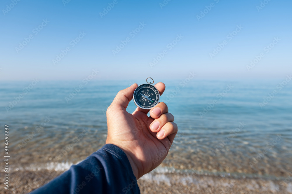 Compass in hand at seacoastA man's hand holds a magnetic compass against the background of a calm morning sea with haze above the water surface Compass in hand at seacoastA man's hand holds a magnetic compass against the background of a calm morning sea with haze above the water surface