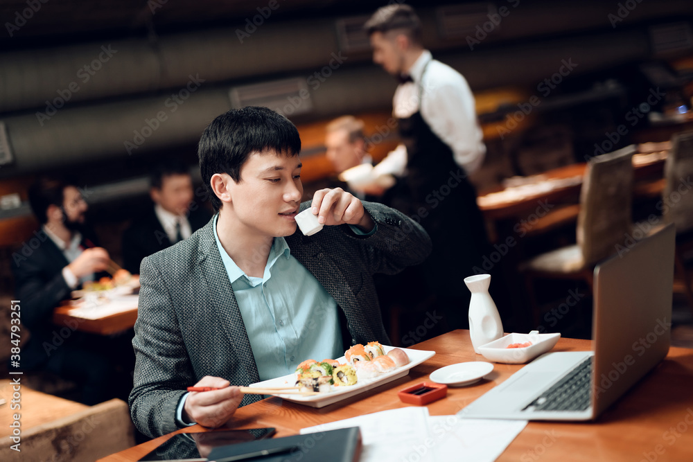 Man drinks coffee eats sushi and works. 