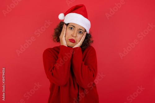 Portrait of beautiful young woman wearing Christmas hat holding head in hands with unhappy expression watching sad movie about animals and trying not to cry.