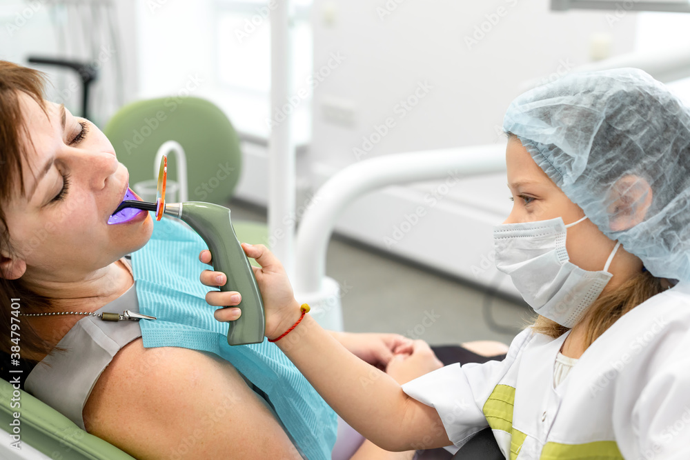 Little girl switched roles with her female dentist. Caucasian child holding lit dental curing UV light in her hands Little girl switched roles with her female dentist. Caucasian child holding lit dental curing UV light in her hands