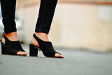 Woman's feet close-up wearing black color high heel shoes and jeans standing on street. with space for text