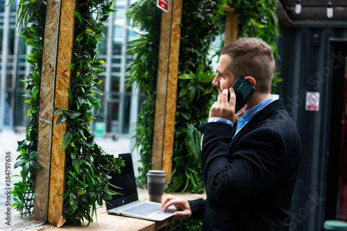 Photo of a young and attractive businessman checking his computer while talking on the phone. Important meeting. Coffee break