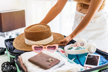 Young woman traveler sitting on the bed packing her suitcase preparing for travel on summer vacation