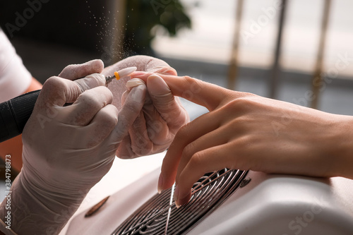Obraz na płótnie A woman manicure master makes a hardware manicure in white gloves removing the old coating of gel Polish in the salon