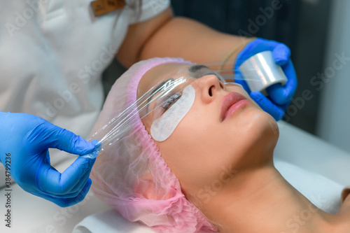 Beautician covered woman lashes file, lift eyelashes procedure, face closeup. Portrait of woman with solution for lamination on lashes. Cosmetologist is making lash lifting in cosmetology clinic.
