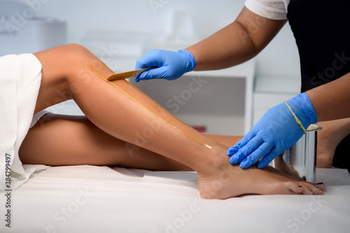 Cosmetologist beautician waxing female legs in the spa center beauty salon cosmetology concept photo
