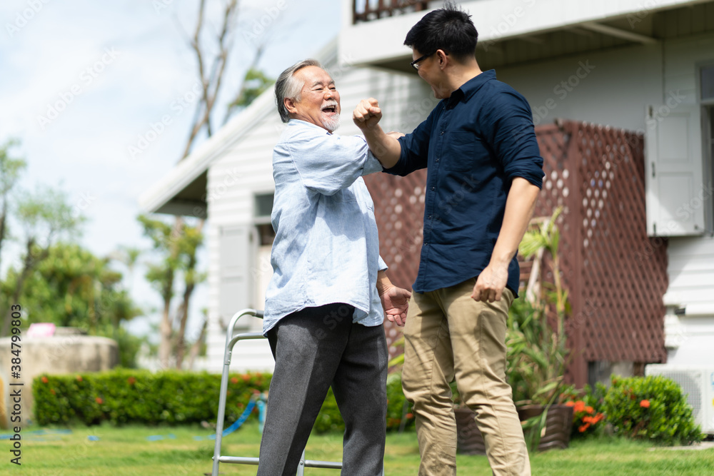 Naklejka premium Elderly Asian father and Adult son walking in backyard. Positive Asian man caregiver helping patient