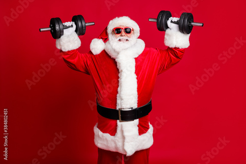 Strongest santa claus. Photo of pensioner old heavyweight man white beard lift dumbbells gritting teeth confirm champion status wear x-mas costume sunglass cap isolated red color background