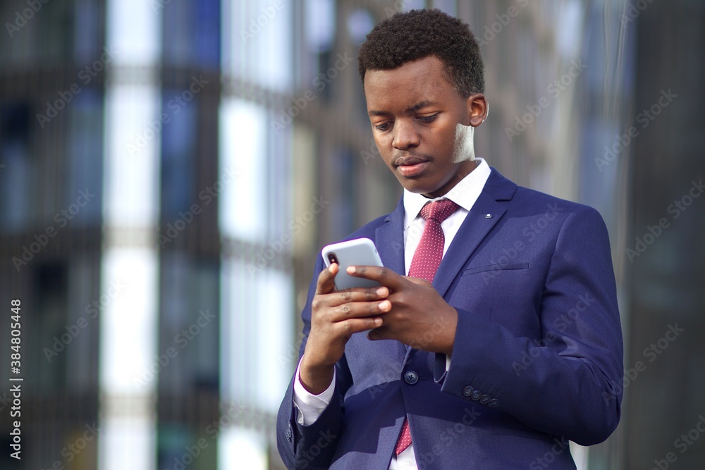 Serious businessman looking at his cell mobile phone, typing a message. Black African Afro American man in suit outdoors with smartphone Serious businessman looking at his cell mobile phone, typing a message. Black African Afro American man in suit outdoors with smartphone