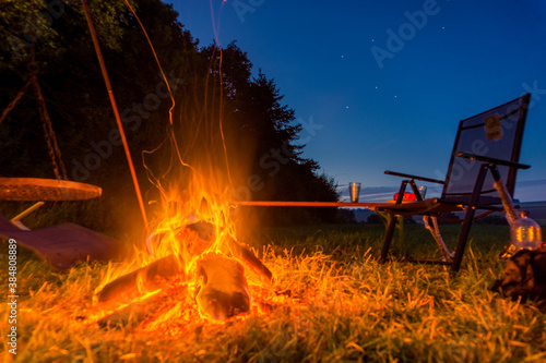 Empty camping chair with bonfire at blue hour and some stars at hte sky