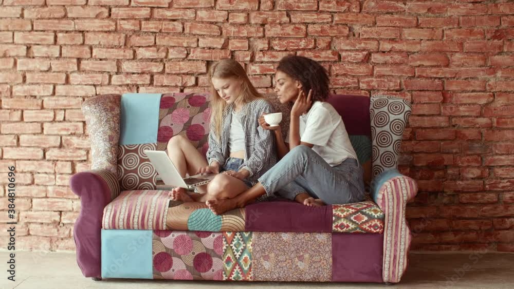 Young beautiful lesbian couple dressed casually enjoy domestic atmosphere surf social network on laptop and drink hot beverage. Modern couple resting together at home Young beautiful lesbian couple dressed casually enjoy domestic atmosphere surf social network on laptop and drink hot beverage. Modern couple resting together at home
