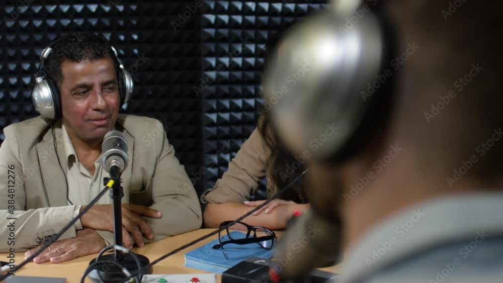 Tracking shot of unrecognizable male radio host in headphones having conversation with cheerful Arab man and Asian woman during live show in studio Tracking shot of unrecognizable male radio host in headphones having conversation with cheerful Arab man and Asian woman during live show in studio