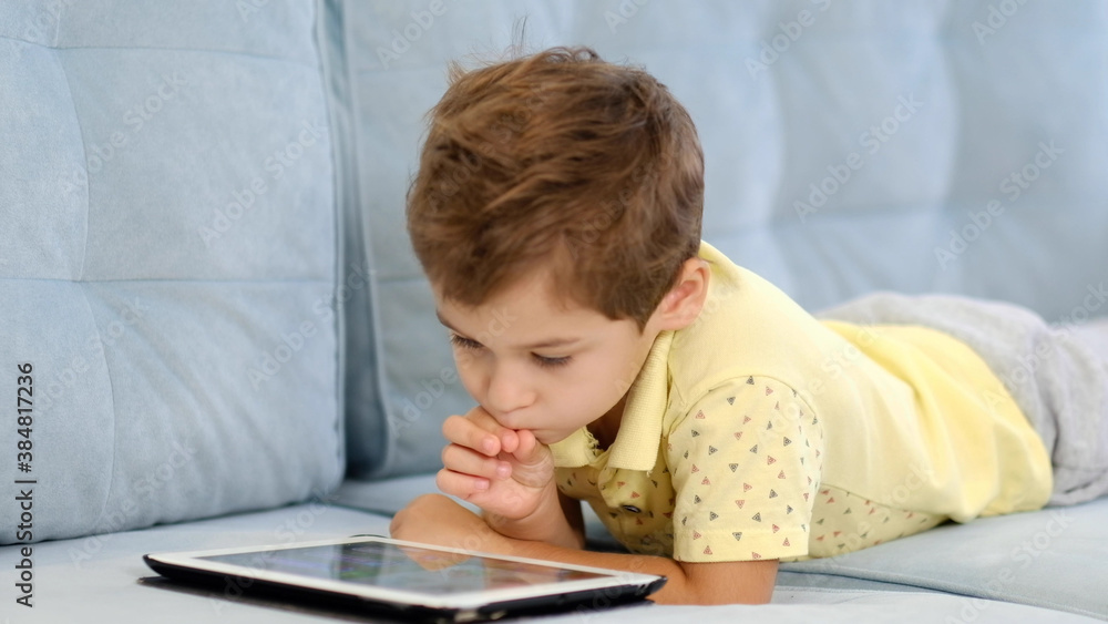 boy home sits on the sofa play looks tablet cartoons games movies movie boy home sits on the sofa play looks tablet cartoons games movies movie