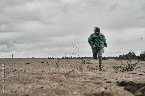 A man walks on the sand in the rain in a green raincoat. Lifestyle