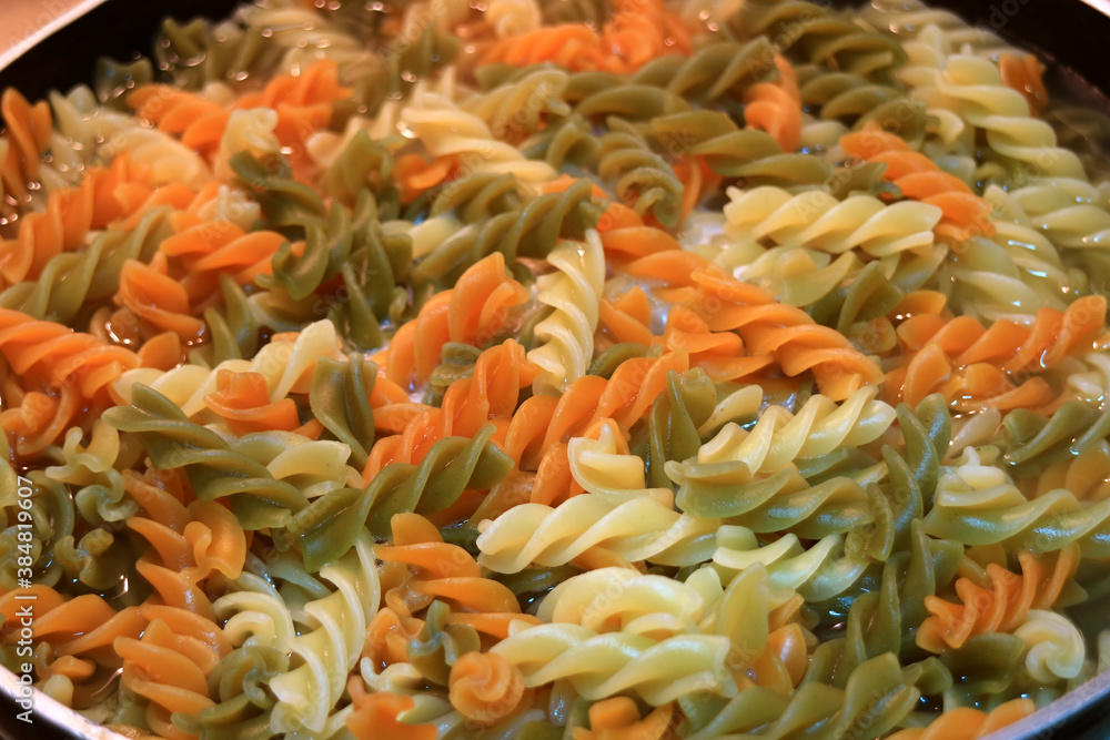 Three-color vegeroni fusilli pasta being boiled in a frying pan, for the concept of EASY HOME-COOKING Three-color vegeroni fusilli pasta being boiled in a frying pan, for the concept of EASY HOME-COOKING