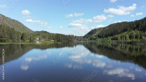 Aerial view between trees, over a calm, reflecting Tovdalelva river, on a sunny day, in Agder,, Norway - dolly, drone shot photo
