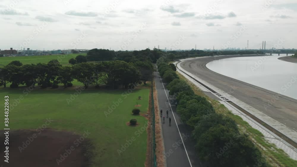 Group Of Cyclists Ride Bikes Along The Arakawa River In Saitama, Japan. - aerial, tracking shot Group Of Cyclists Ride Bikes Along The Arakawa River In Saitama, Japan. - aerial, tracking shot