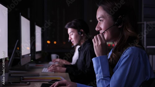 3 pepople, Late night shift call center business concept. Beautiful female Asian customer service on headphone, working, smiling, talking, pleased to service, among blurry background of coleagues photo