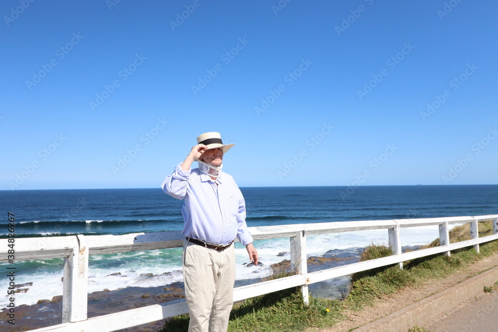 Beach life. Man with neck injury wearing neck guard support and white hat is alone strolling by the beach in a hot sunny day. Beach life. Man with neck injury wearing neck guard support and white hat is alone strolling by the beach in a hot sunny day.