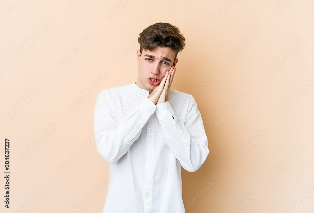 Young caucasian man isolated on beige background yawning showing a tired gesture covering mouth with hand. Young caucasian man isolated on beige background yawning showing a tired gesture covering mouth with hand.