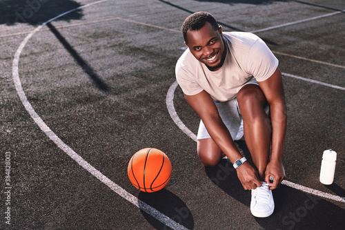 Joyful man tying his shoelaces on a basketball court