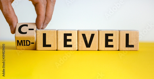 From mid level to C level. Hand turns a cube and changes the words 'mid level' to 'C level'. Beautiful yellow table, white background, copy space. Business concept. photo