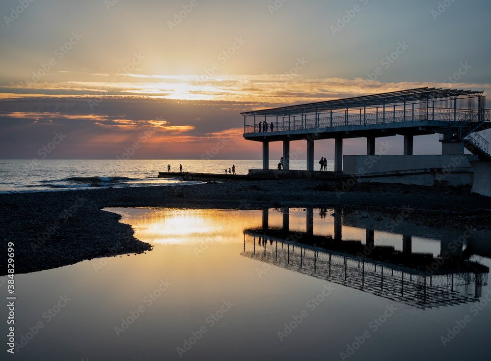 Silhouettes of people and pier at sunset and calm sea water background