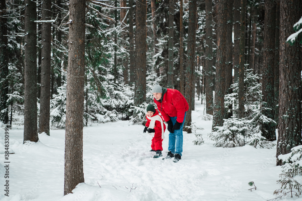 In winter, in the woods, a man in a jacket plays outdoor games with his son in overalls to keep warm.