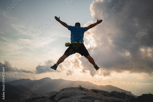 Hiker jumps and enjoys a stunning sunset from the peak of a mountain
