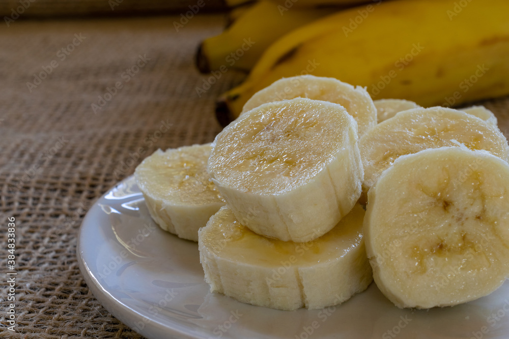 closeup of a sliced ​​banana on the plate and a bunch of bananas in the background. selective focus and space for text.