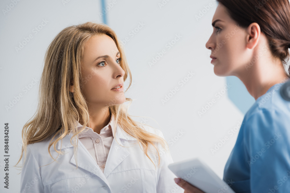Selective focus of doctor looking at pensive nurse with digital tablet in clinic Selective focus of doctor looking at pensive nurse with digital tablet in clinic
