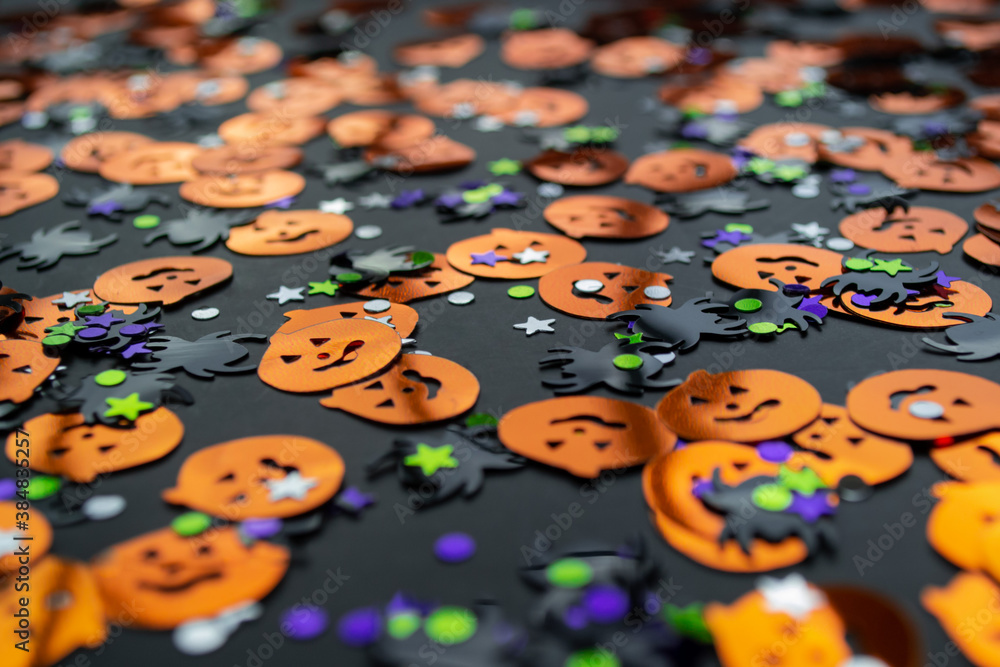 Halloween background: shiny confetti in the shape of orange pumpkins, black spiders and colorful stars green, purple color Halloween background: shiny confetti in the shape of orange pumpkins, black spiders and colorful stars green, purple color
