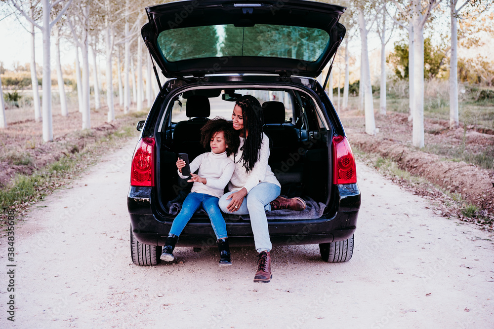 hispanic mother and afro kid girl sitting in a car in nature. Autumn season. Family and travel concept