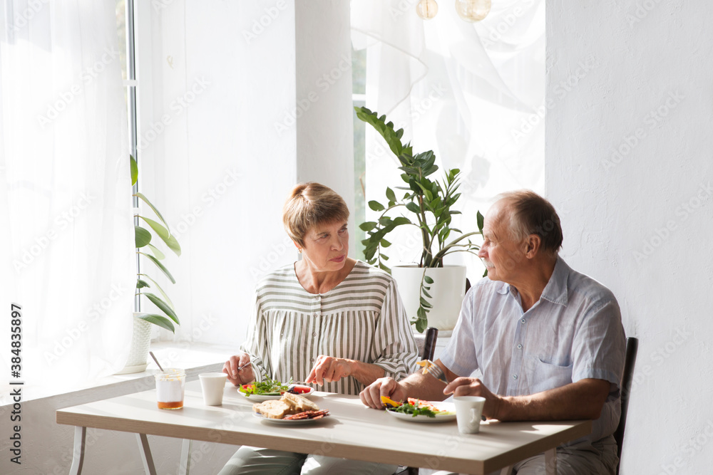 Portrait of relaxed fun senior couple together and eating breakfast in their kitchen at home
Portrait of relaxed fun senior couple together and eating breakfast in their kitchen at home