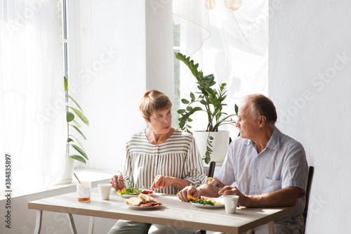 Portrait of relaxed fun senior couple together and eating breakfast in their kitchen at home 