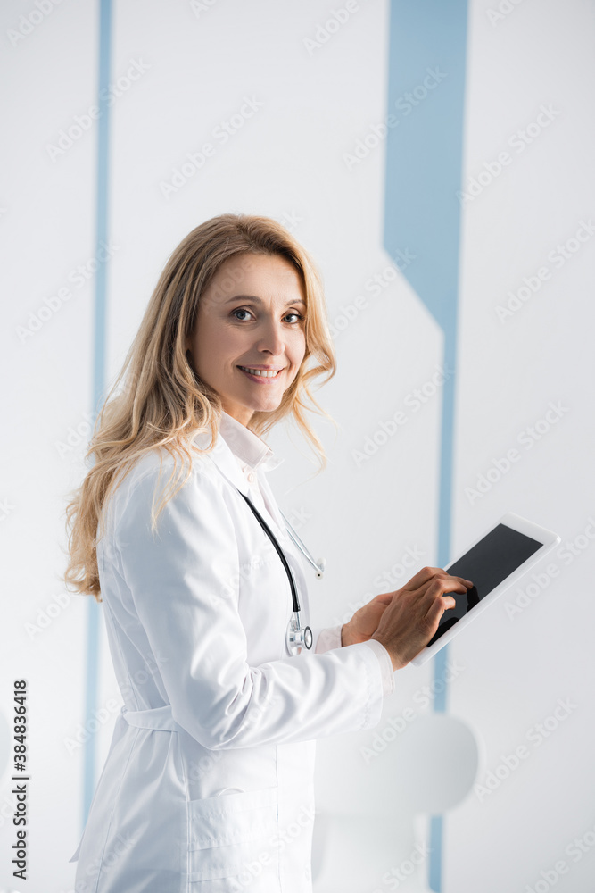 Side view of doctor looking at camera while using digital tablet