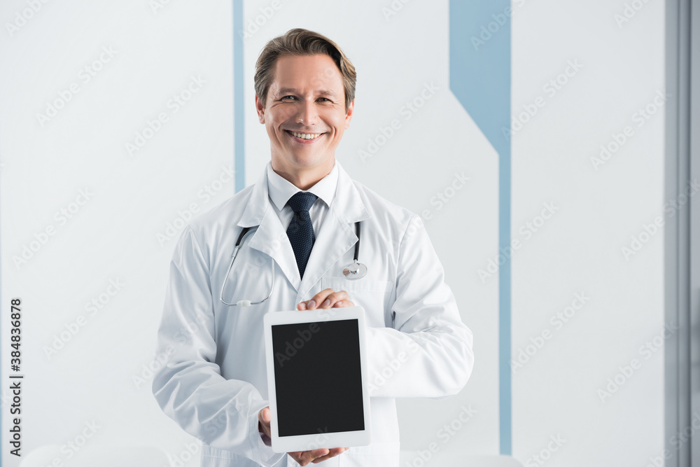 Doctor in white coat looking at camera and showing digital tablet with blank screen in hospital Doctor in white coat looking at camera and showing digital tablet with blank screen in hospital