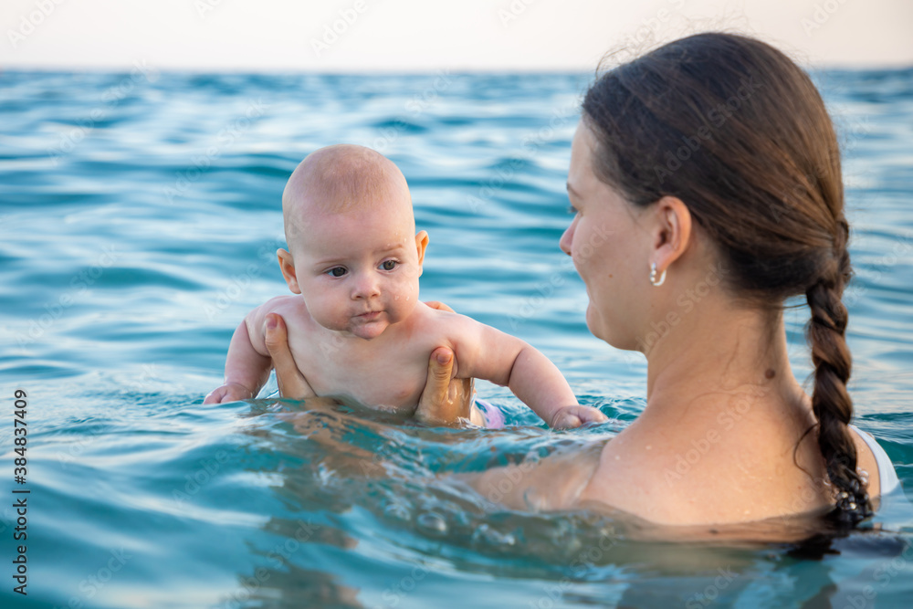 Beautiful young woman with her daughter little baby girl swimming and relaxing in the sea at sunset time Beautiful young woman with her daughter little baby girl swimming and relaxing in the sea at sunset time