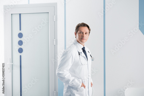 Doctor with hands in pockets of white coat looking at camera in clinic