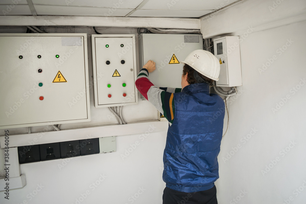 Fotografie An electrician in an engineering helmet opens the switch box