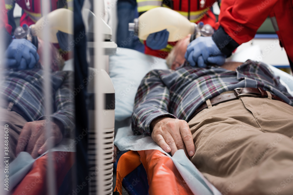Selective focus of elderly patient lying in ambulance car while paramedics doing cardiopulmonary resuscitation